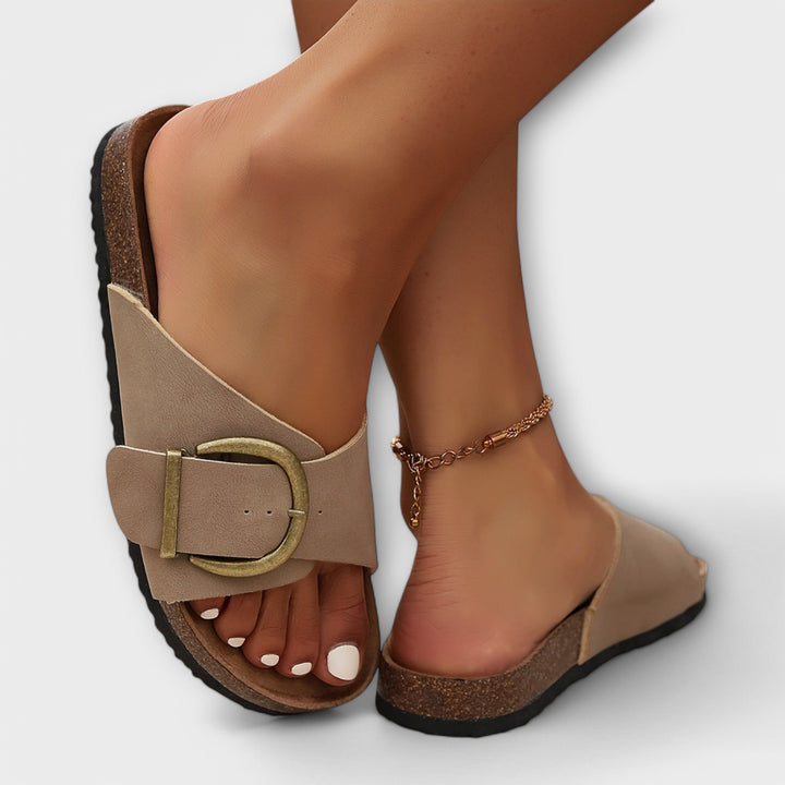 Woman standing in chic slip-on sandals on a plain background.