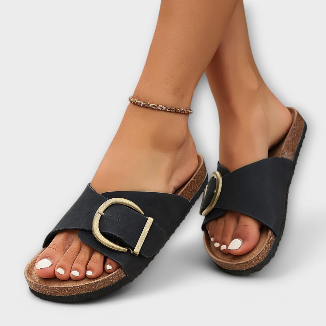 Woman wearing stylish buckle sandals on a plain background.