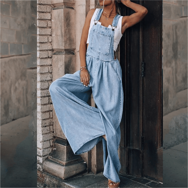 Woman wearing a flowy denim jumpsuit with button bib detail on a plain background.