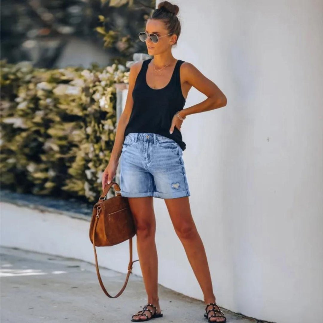 Woman in stylish high waist shorts paired with a casual top on a plain background.