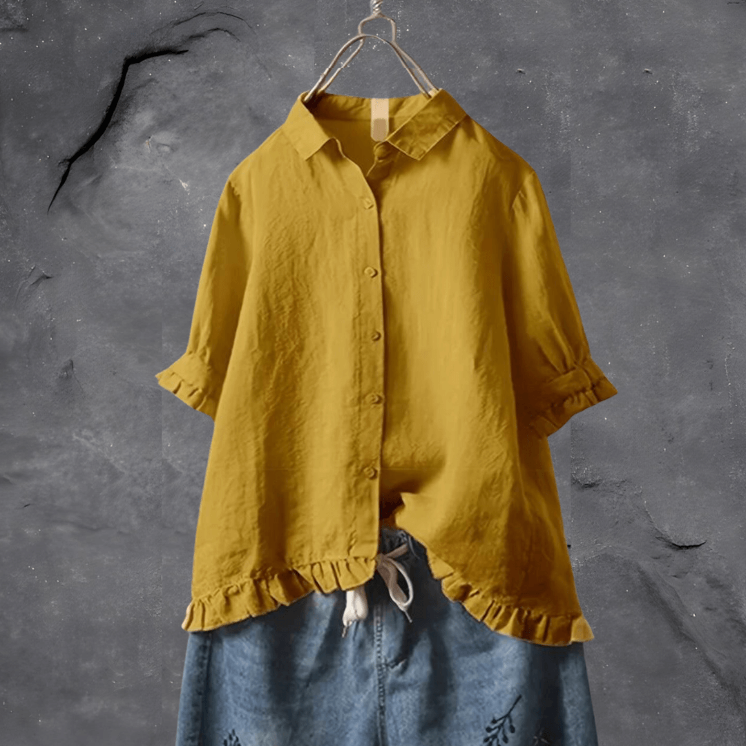 Female wearing a flowing blouse with subtle detailing on a plain background.