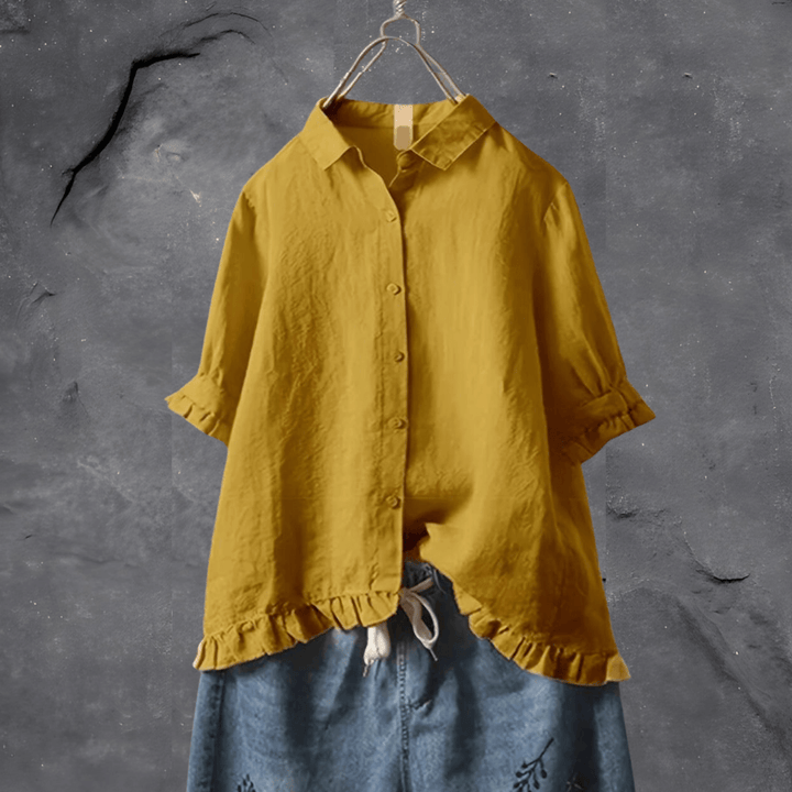 Female wearing a flowing blouse with subtle detailing on a plain background.