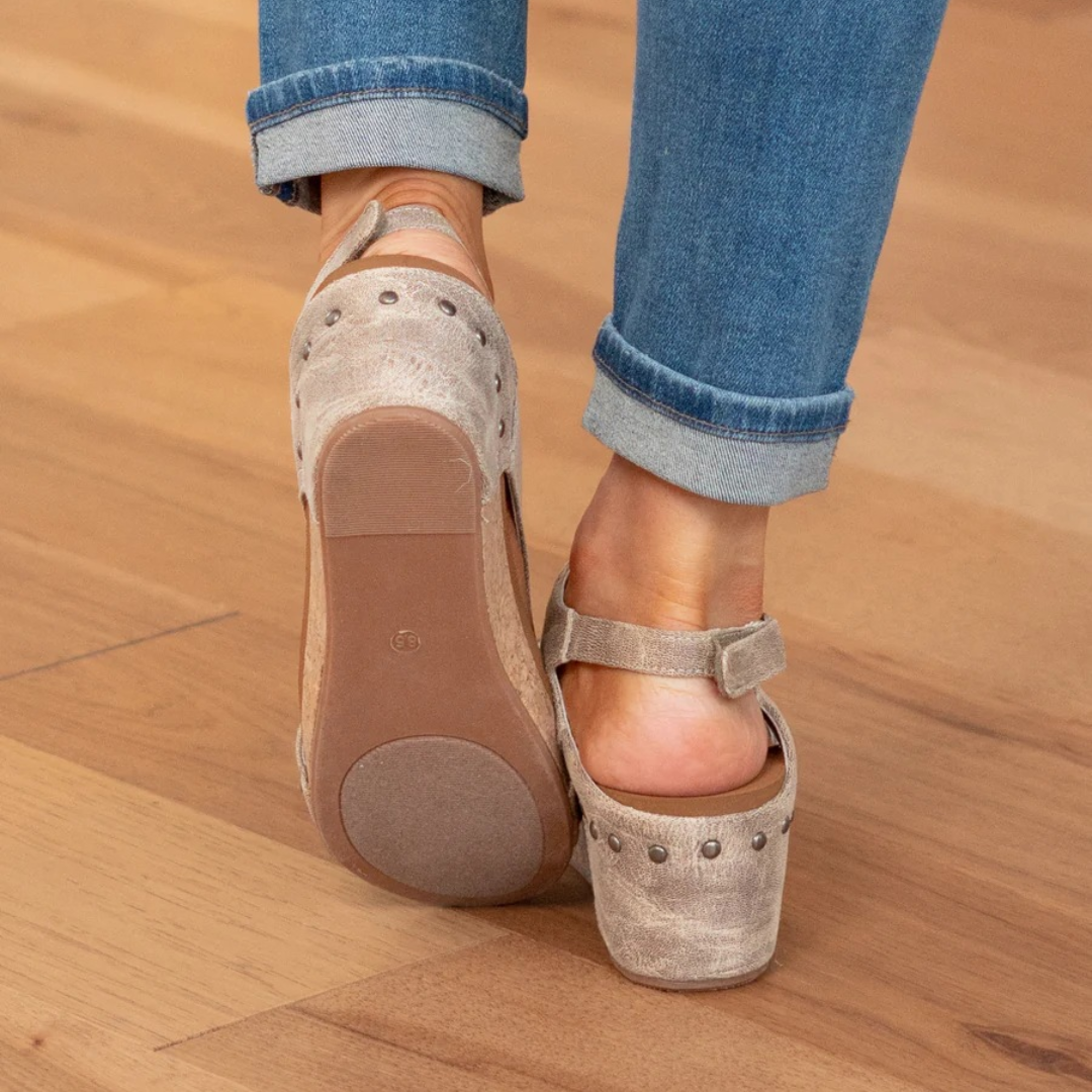 Female model wearing chic summer wedge sandals on a plain background.