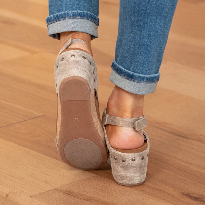 Female model wearing chic summer wedge sandals on a plain background.