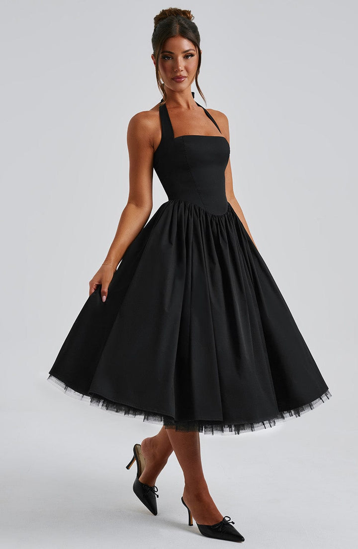 Woman in an occasion halter dress with midi length against a plain background.