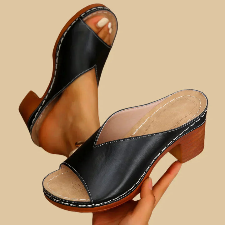Female model posing in chunky heel sandals on a plain background.