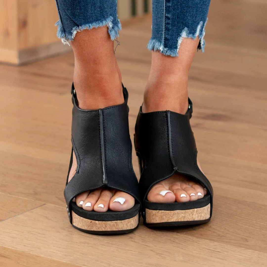 Woman posing with closed-front sandals and open heel on a plain background.