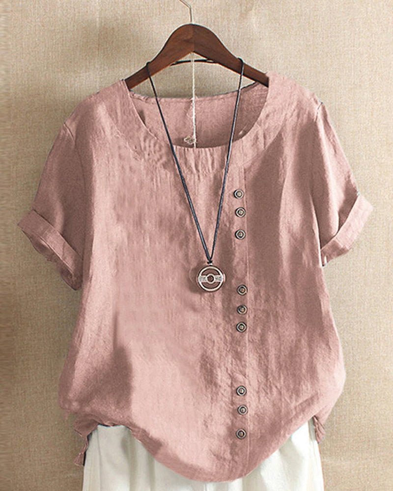 Woman wearing a button front top with cuffed short sleeves against a plain background.em.