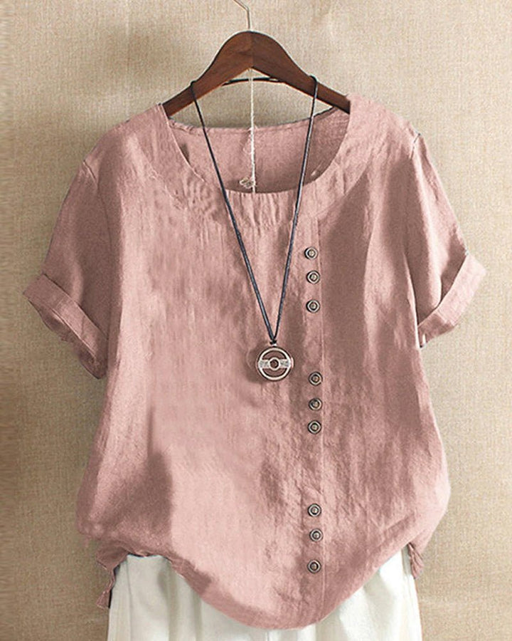 Woman wearing a button front top with cuffed short sleeves against a plain background.em.