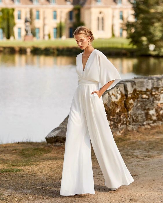 Female model wearing a wide leg jumpsuit with flowing sleeves on a nature background.