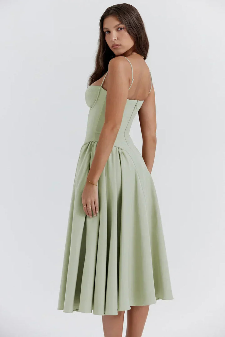 Female model in a pleated midi dress with a defined waist on a plain background.