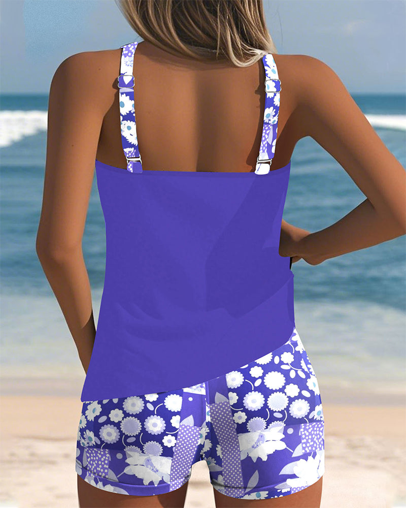 Female model wearing a tank-style swim top and floral shorts on a beach background.