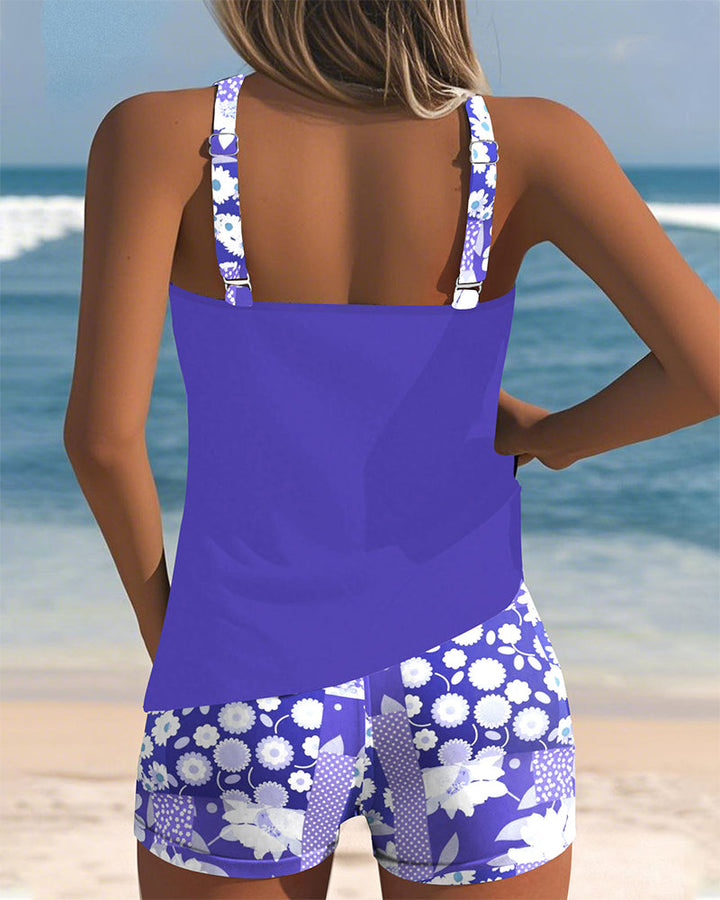 Female model wearing a tank-style swim top and floral shorts on a beach background.