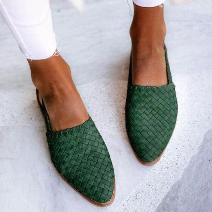 Female model wearing woven ballet flats with a rounded toe on a plain background.