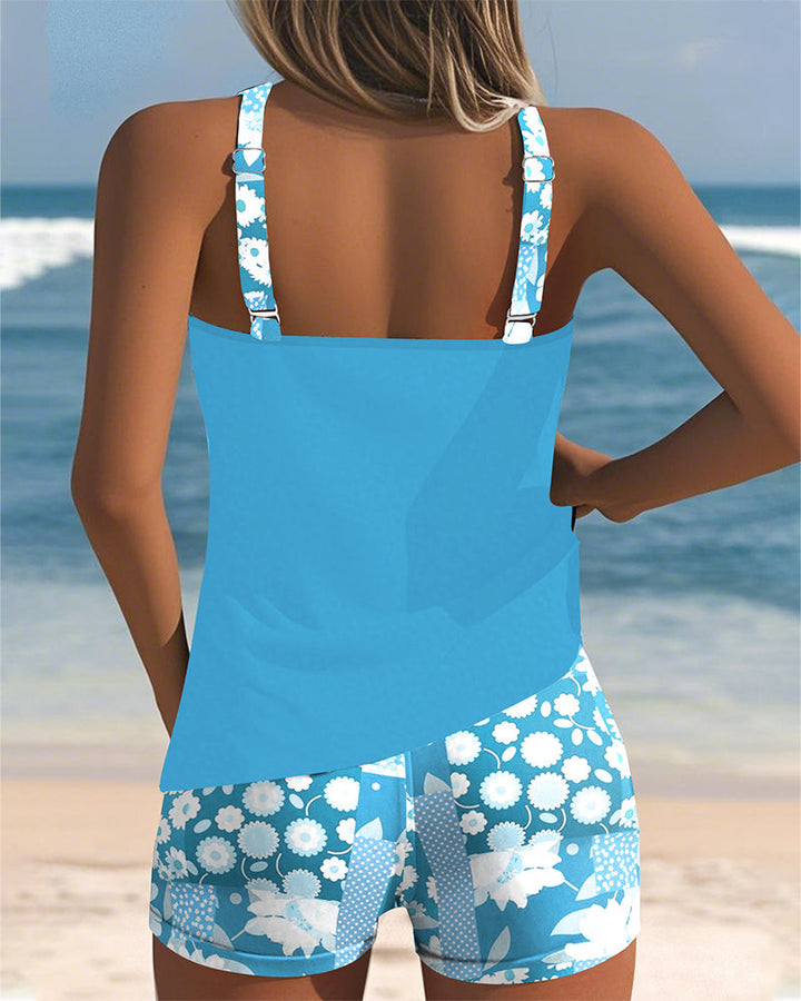 Female model in a tankini top and printed swim shorts on a beach background.