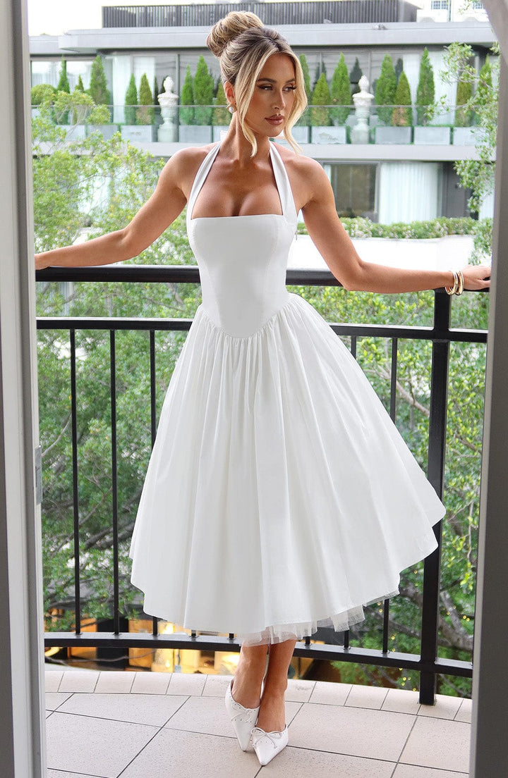 Woman in a summer halter midi dress shown on a terrace background.