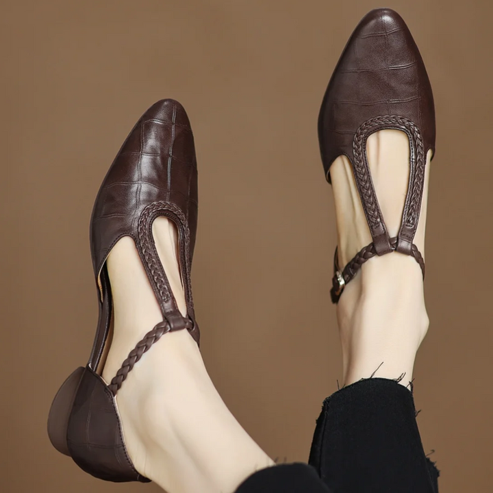 Women’s T-strap Mary Jane flat shoe on a plain background with a softly pointed toe and braided strap.