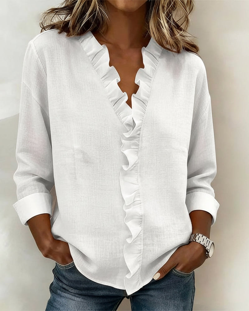  Female modelling a flowing blouse with ruffle neckline detailing on a plain background.