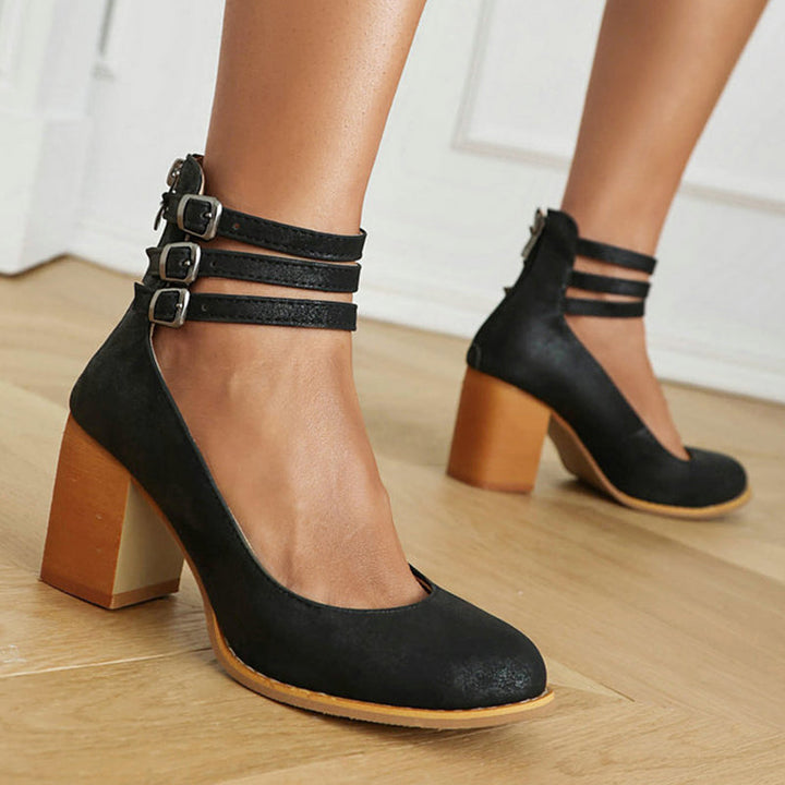 Woman showcasing simple block heel sandals against a plain background.