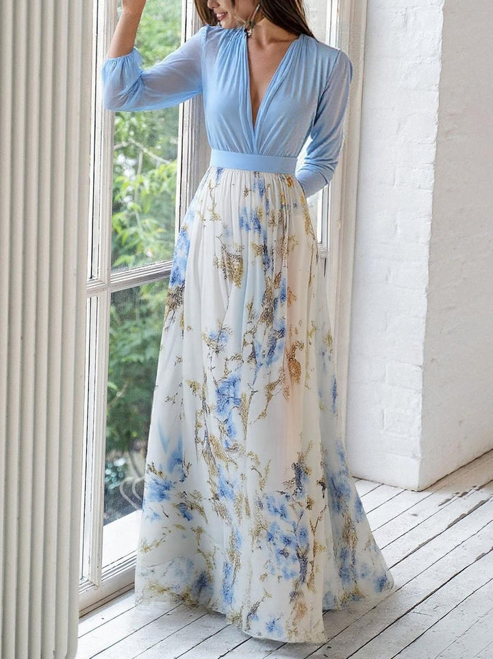 Woman styled in a flowing floral maxi dress with a fitted waist on a plain background.