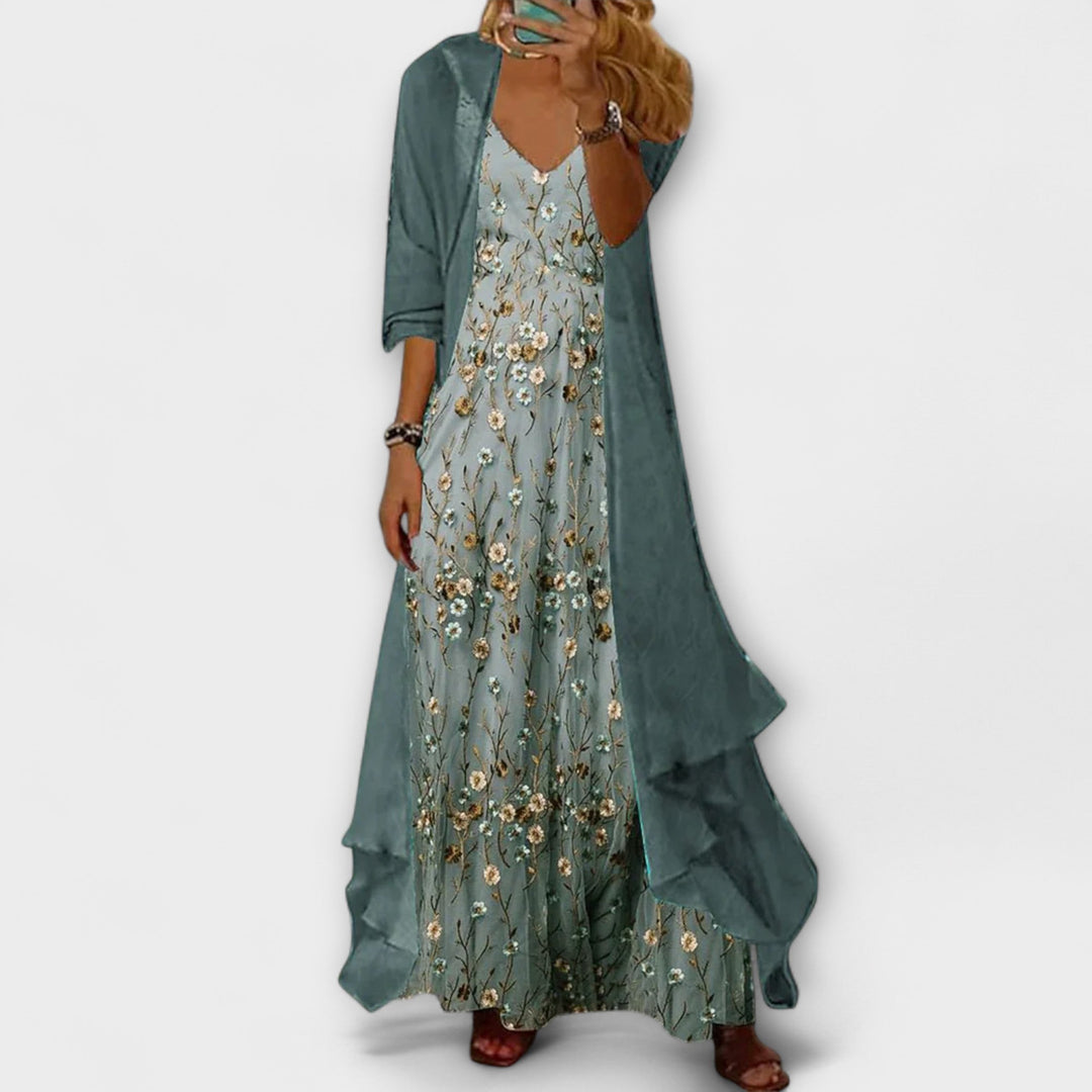 Woman in a two-piece floral outfit featuring a maxi dress and open-front jacket on a plain background.