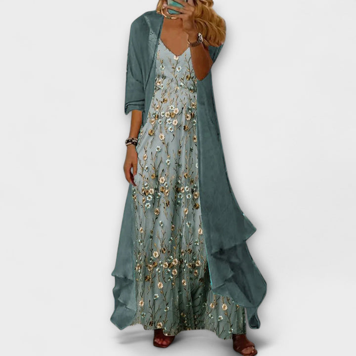  Woman in a two-piece floral outfit featuring a maxi dress and open-front jacket on a plain background.