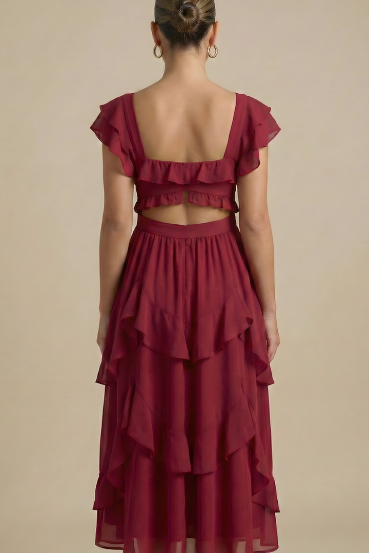 Woman posing in a flowing midi dress with tiered skirt details against a plain background.