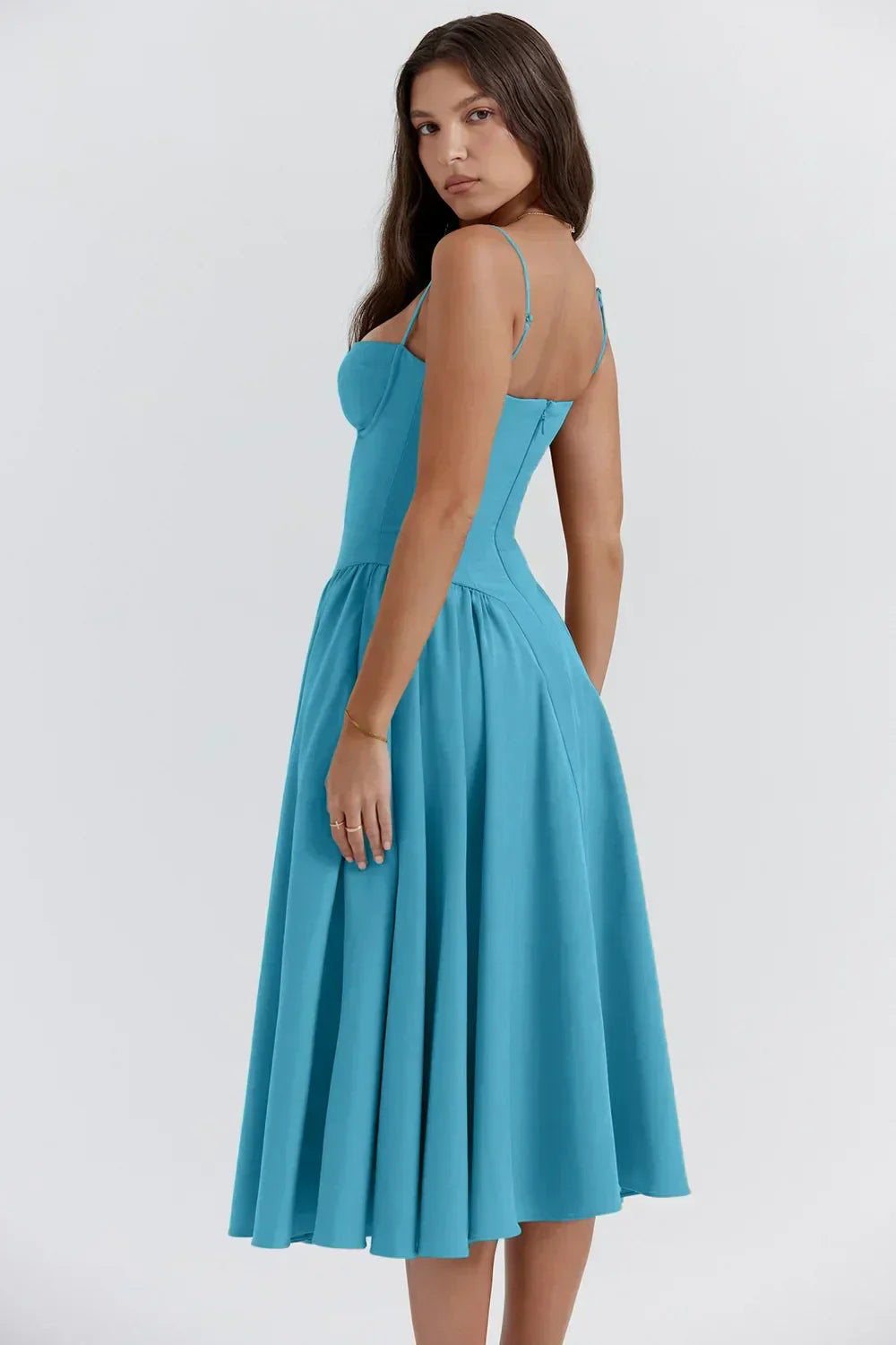 Woman wearing a sleeveless dress with a softly gathered waist on a plain background.