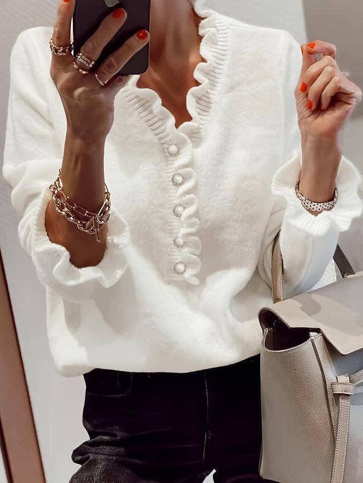 Female model wearing a ruffle blouse with button details on a plain background.