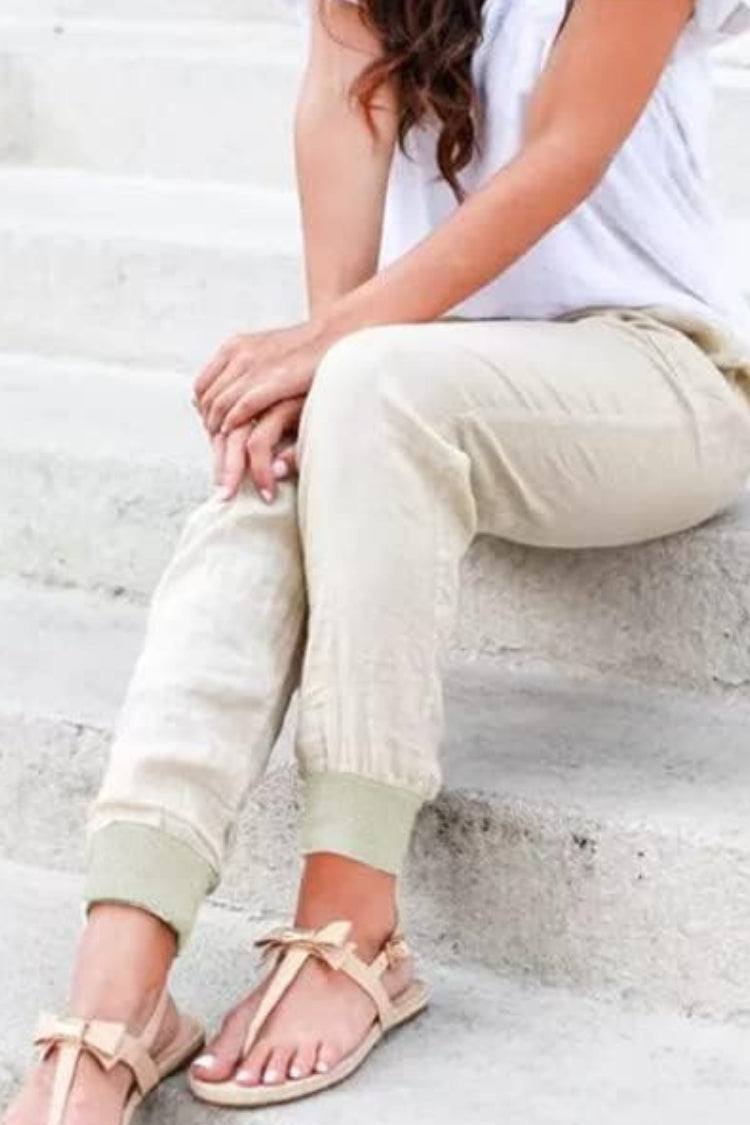 Woman in relaxed ankle-length trousers with elastic cuffs and side pockets on a plain background.
