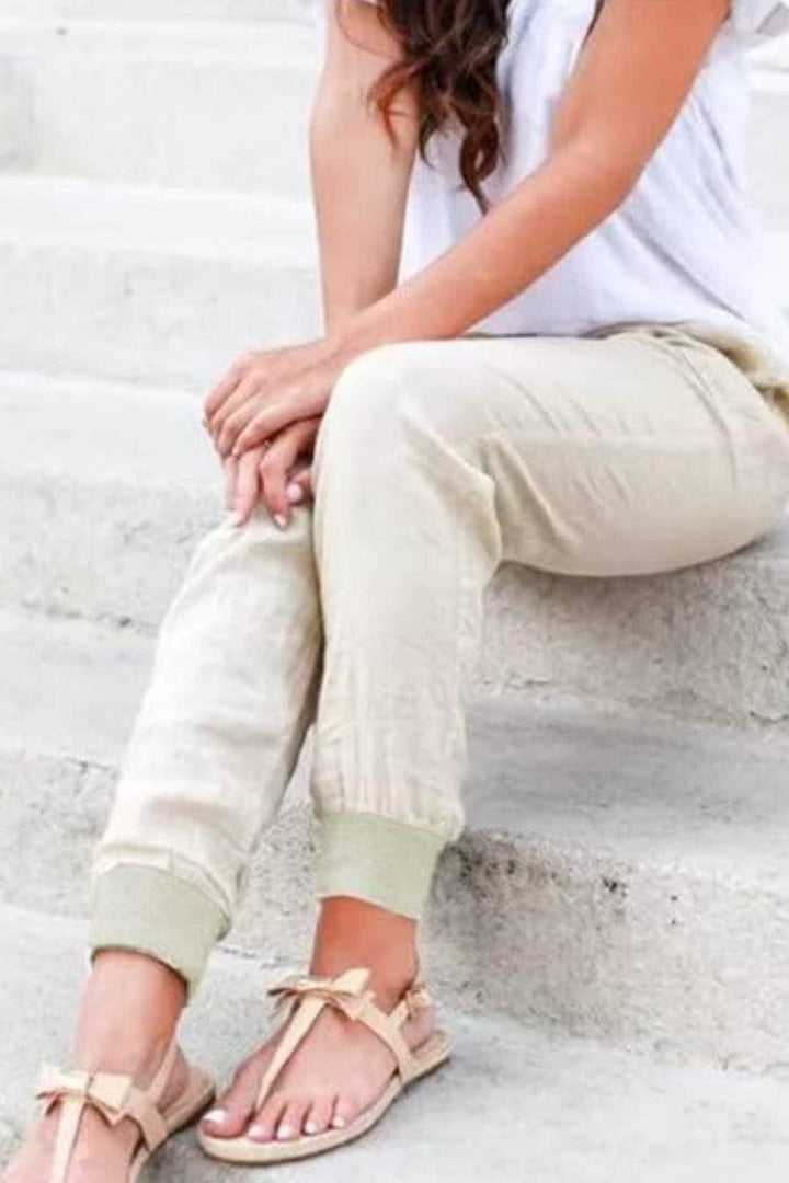 Woman in relaxed ankle-length trousers with elastic cuffs and side pockets on a plain background.