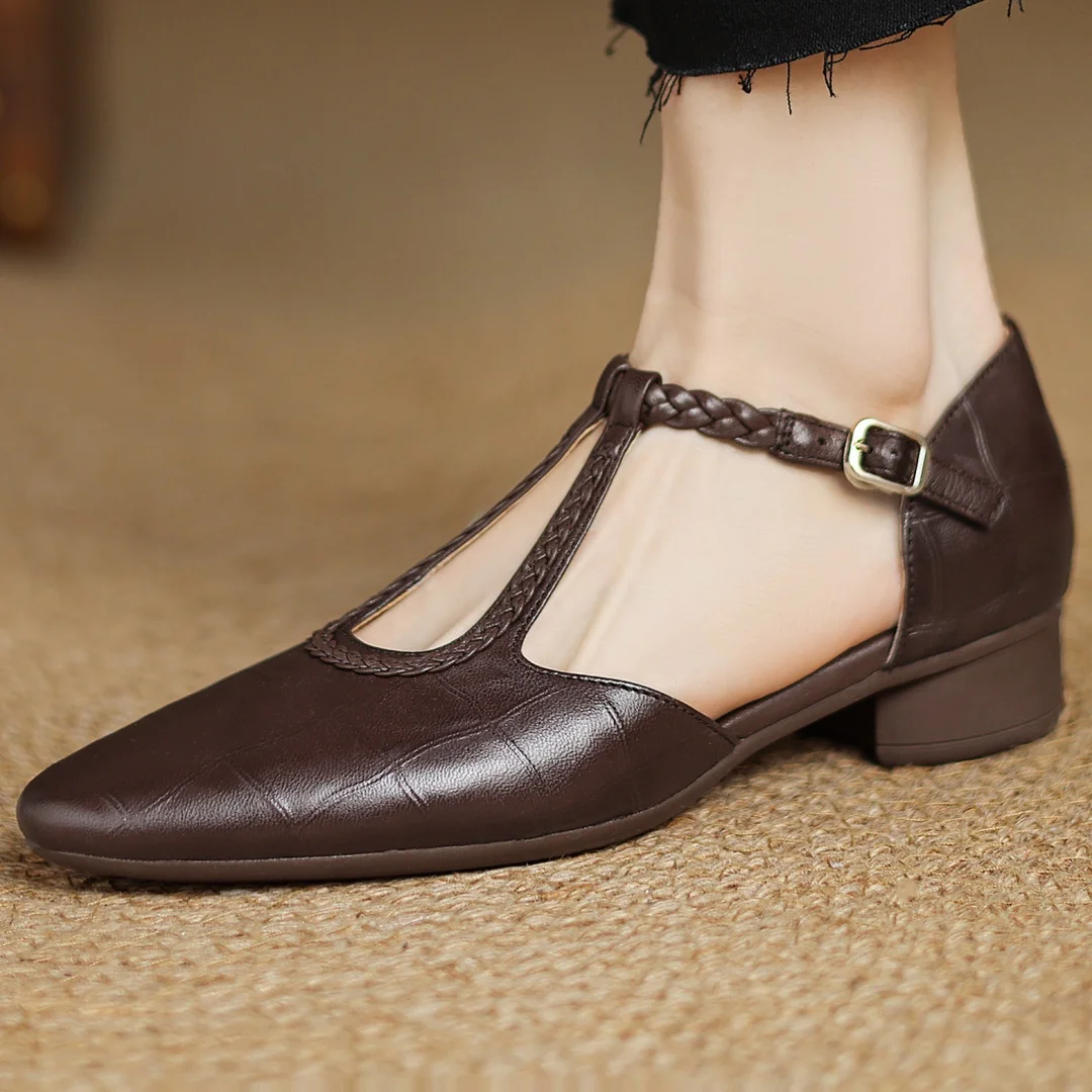 Dark brown women’s flat shoe with slim T-strap detail displayed on a plain background.