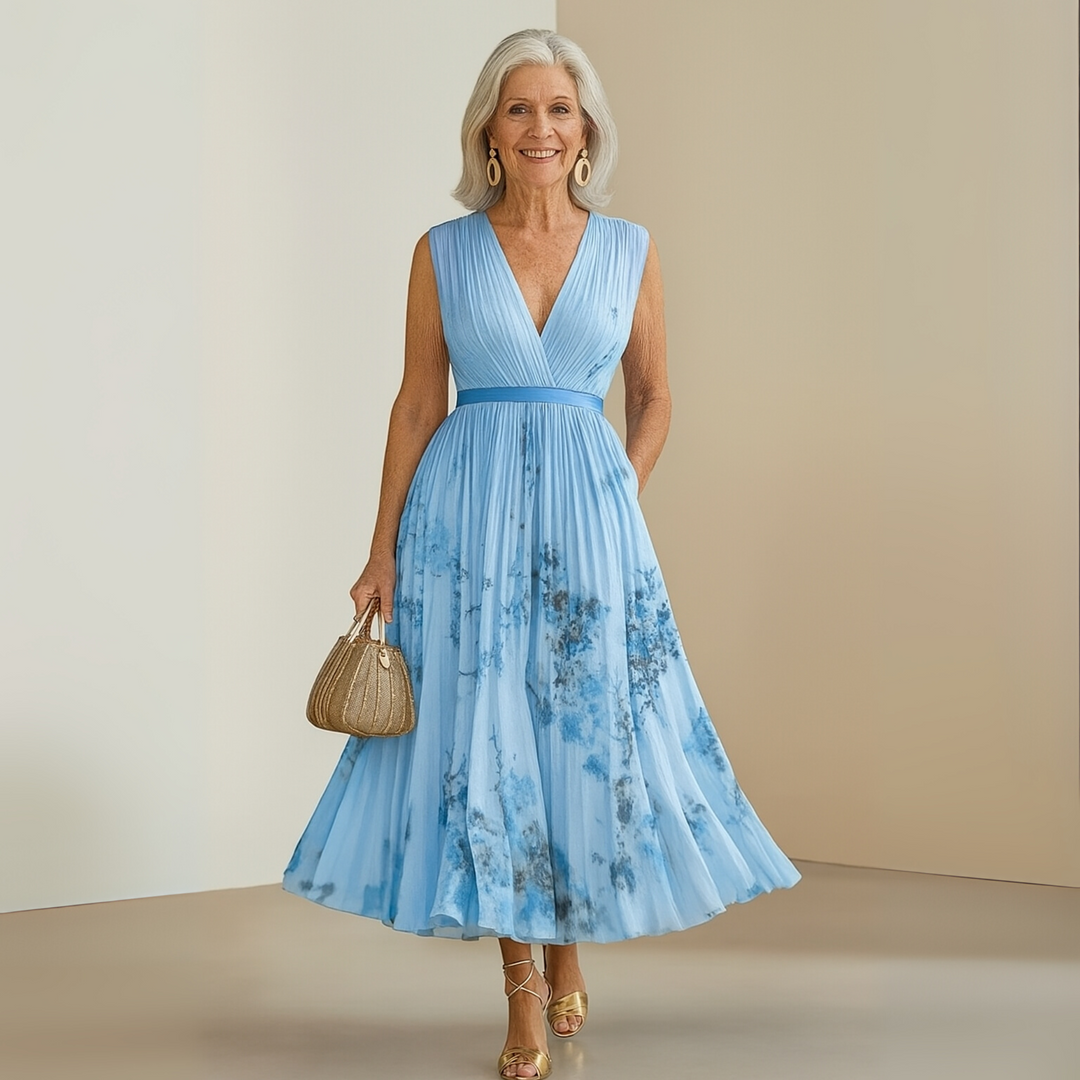 Female wearing a long dress with a defined waist and flowing pleated skirt.