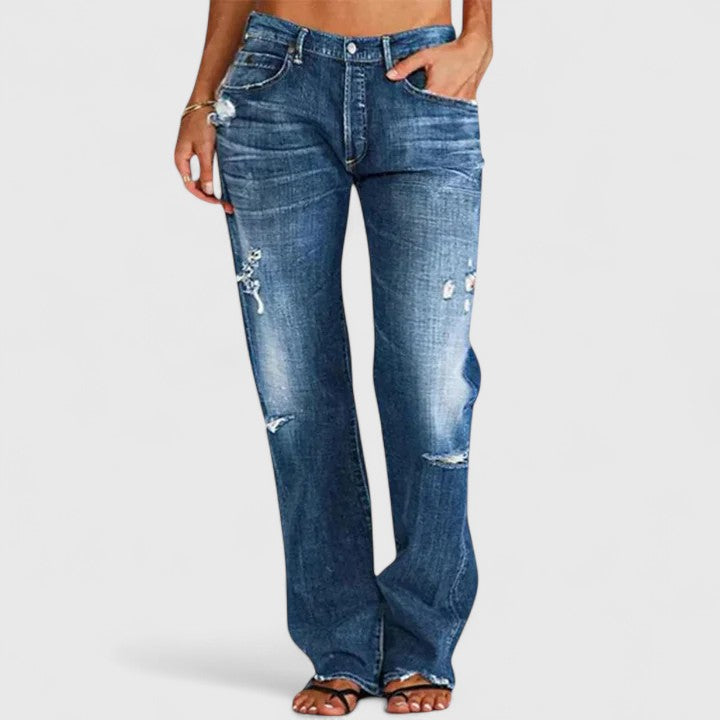Female model wearing low-rise flare jeans with distressed detailing against a plain background.