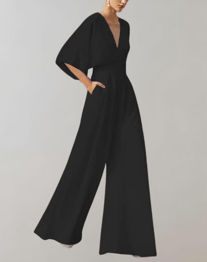 Woman wearing a dressy jumpsuit with wide legs and soft sleeve drape on a plain background.