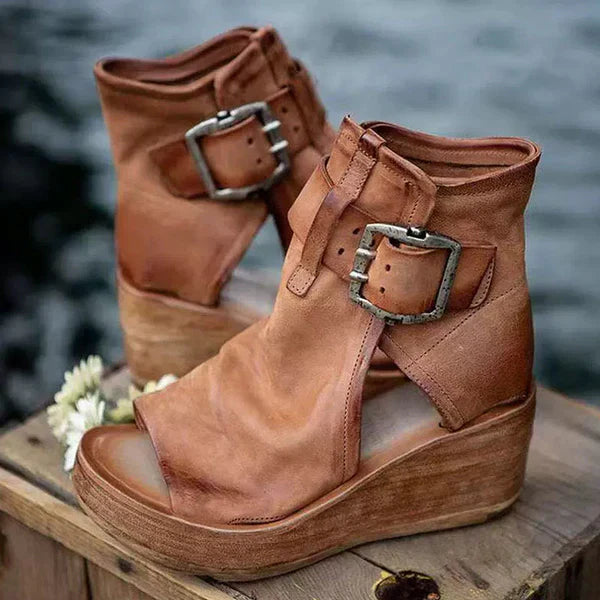 Woman wearing adjustable buckle wedge sandals with a plain background.