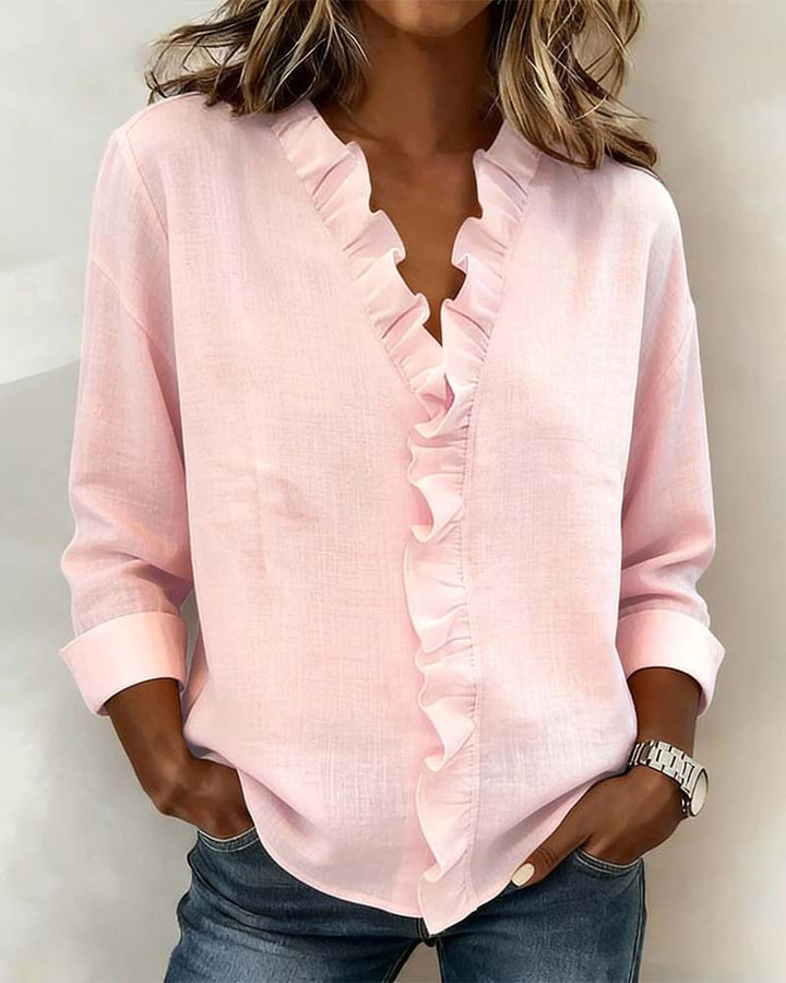 Woman wearing a long sleeve ruffle blouse with a V-neckline against a plain background.
