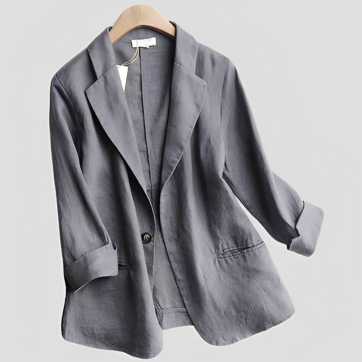 Woman showcasing a tailored blazer with three-quarter sleeves on a plain background.