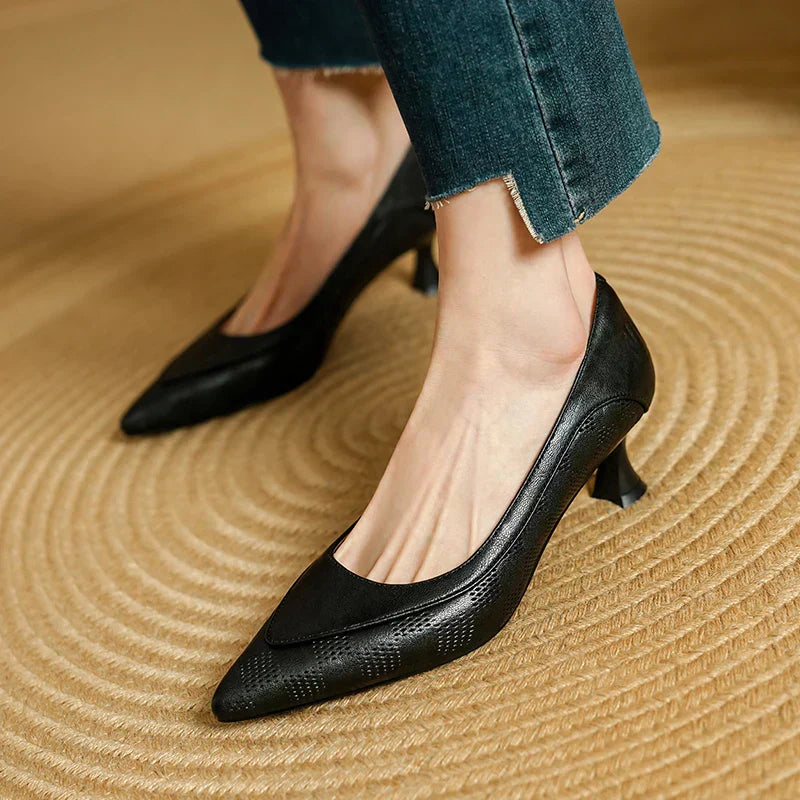 Female model showcasing low heel dress shoes on a plain background.
