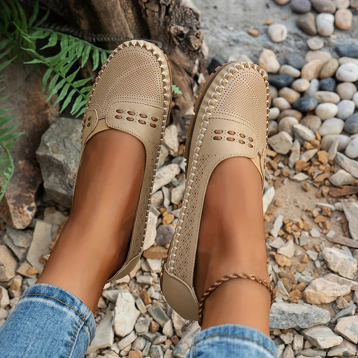 Female model showing casual flats on a plain stone background.