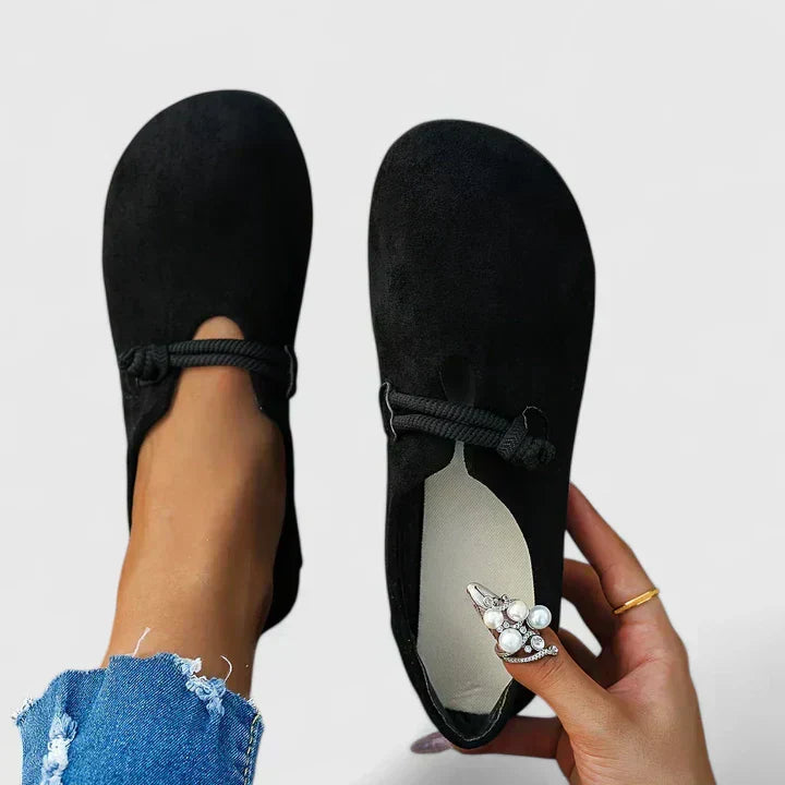 Woman showcasing classic slip-on shoes with a plain background.