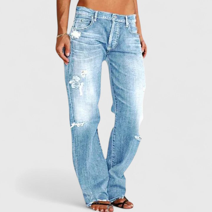 Woman wearing low-rise jeans with a dramatic flare leg against a plain backdrop.