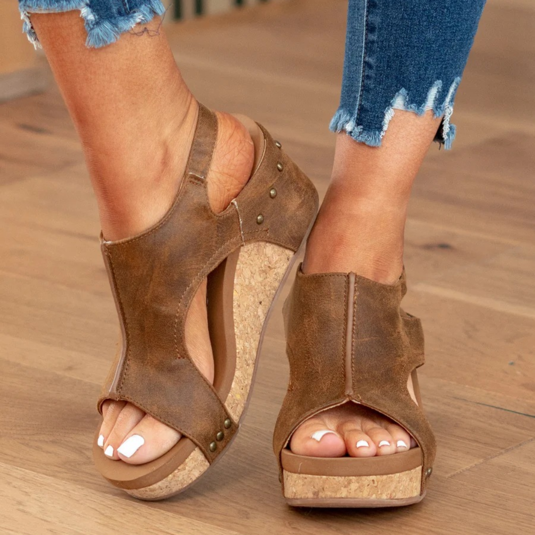 Woman showcasing feminine wedge sandals against a plain background.