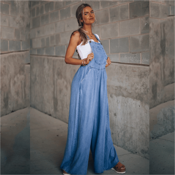 Woman styled in a loose denim dungaree jumpsuit against a plain background.