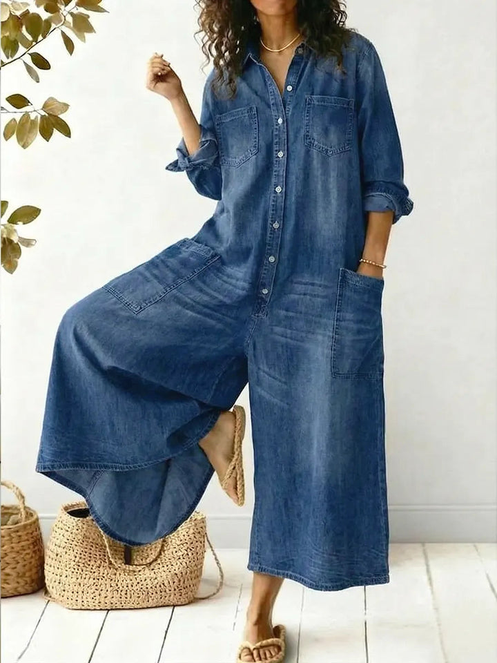 Woman wearing a relaxed denim jumpsuit with a button-front top against a plain background.