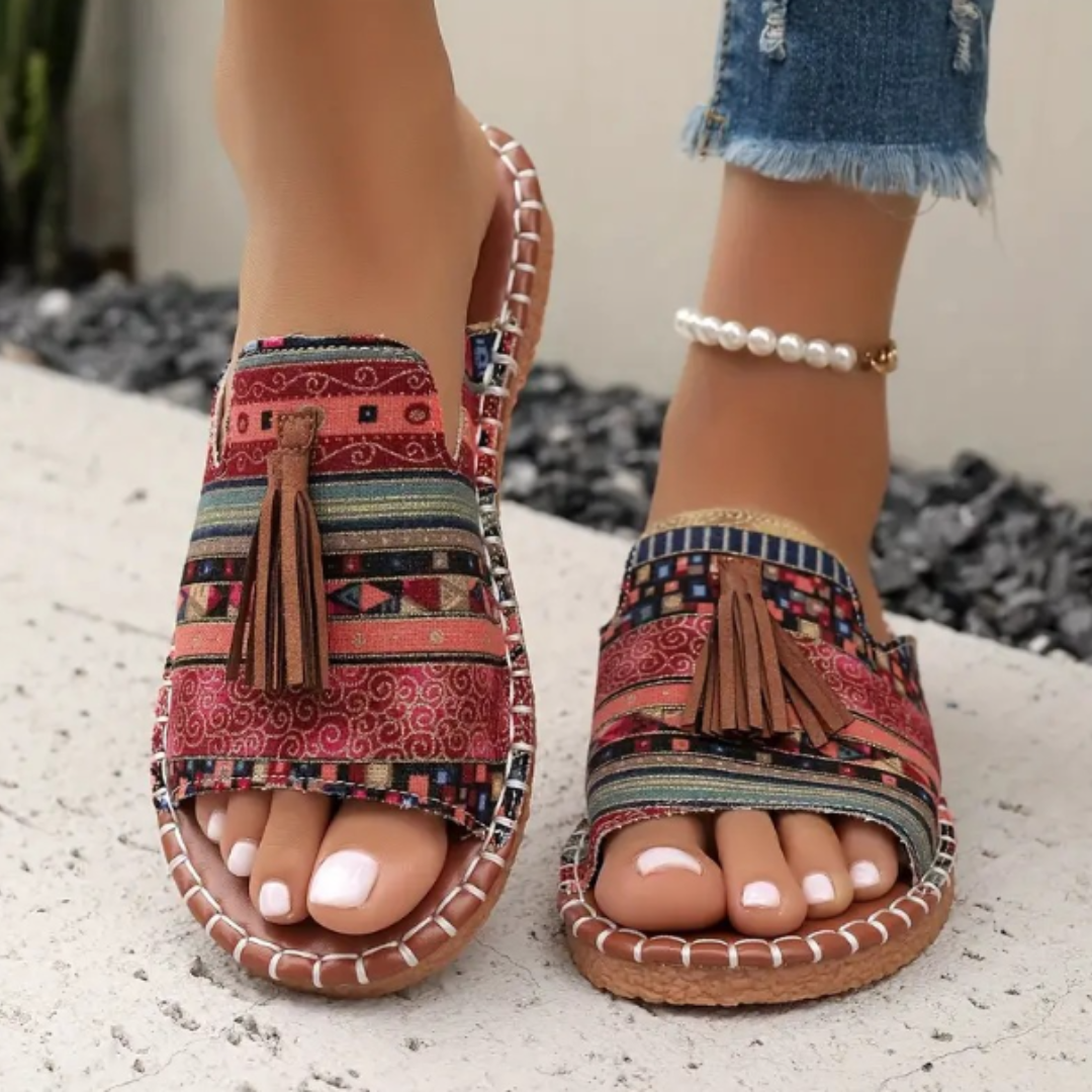 Female model wearing colorful slip-on sandals on a plain background.