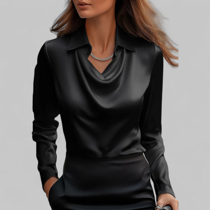 Woman wearing a long sleeve blouse with flowing drape detail against a plain backdrop.