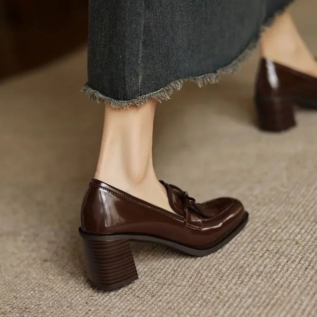 Female wearing glossy round toe loafer pumps with block heels on a plain background.