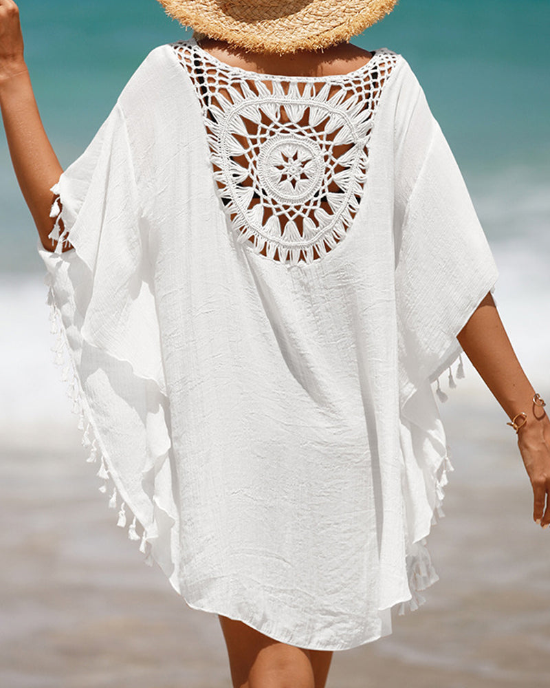 Woman wearing a boho crochet beach cover up with tassel hem on a plain background.