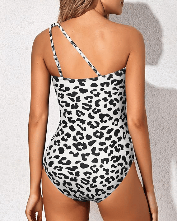Model wearing a sleek one shoulder bathing suit on a plain background.